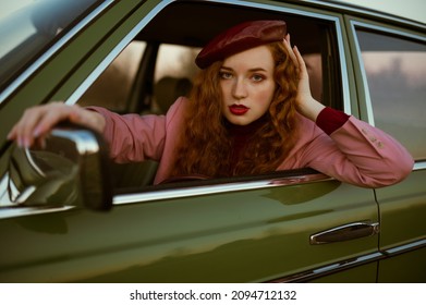 Fashionable elegant confident redhead woman with marsala color lips, eyes makeup, wearing faux leather beret, classic pink blazer, posing, sitting in the green vintage car