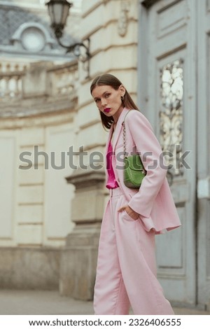 Fashionable elegant confident woman wearing trendy pink suit blazer, wide trousers, with green faux leather shoulder bag, walking in street. Outdoor fashion portrait