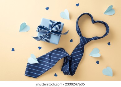 Fashionable Father's Day concept. Top-down view of a gift box, necktie, and hearts on a pastel beige background