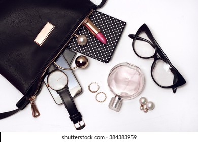 Fashionable female accessories watch glasses lipstick perfume and black bag. Overhead of essentials for any girl