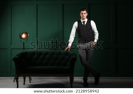 Fashionable gentleman standing near sofa in dark room