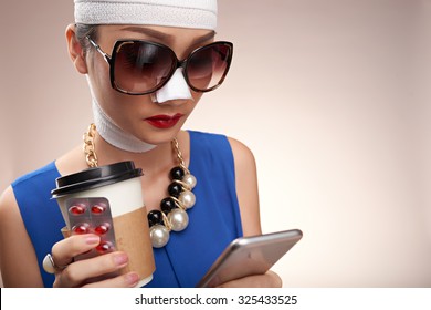 Fashionable girl with bandage on her face reading message in her smartphone