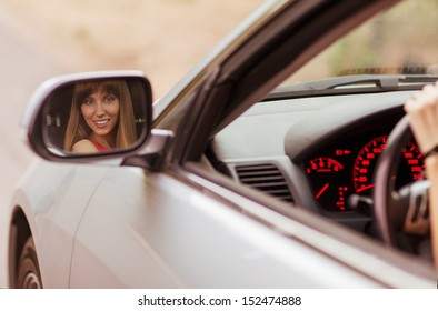 Fashionable Girl Sitting In A Gray Car. Her Smiling Face Reflected In The Side Mirror.