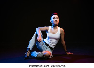 Fashionable Girl With Stylish Haircut Posing On Black Background With Trendy Colored Light. Face Girl With Bright Makeup In White T-shirt And Blue Jeans. Beautiful Confident Woman With Bold Eyeliner