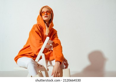 Fashionable girl wearing orange hoodie, glasses looking up,  posing on white background. Copy, empty space for text - Shutterstock ID 2120664530