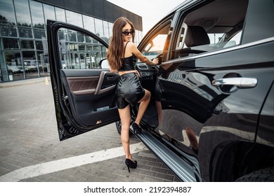 Fashionable Glamorous Asian Woman Getting Into The Big Luxury Car. She Is Wearing Black Leather Top And Shorts, High Heels, Looking At Camera.