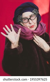 Fashionable Grandmother In Turban, Glamorous Glasses Greets With Hand. Older Woman Fashionista. Fashion For The Elderly Woman. Trendy People. Elegant Granny In Faux Fur Coat. Old Woman In Winter Trend