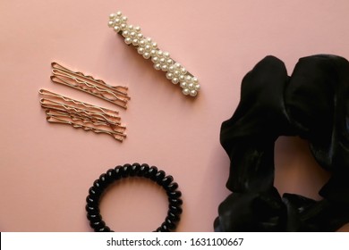 Fashionable hair accessories on pastel pink background; black scrunchie, goldenhair pins, coil hair tie and beret with pearls. Top view.