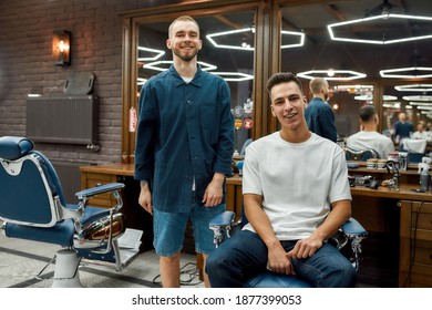 Fashionable hairstyle. Portrait of cheerful barber and his young client looking at camera and smiling. In barbershop. New haircut. Young man visiting barbershop. Mens haircut