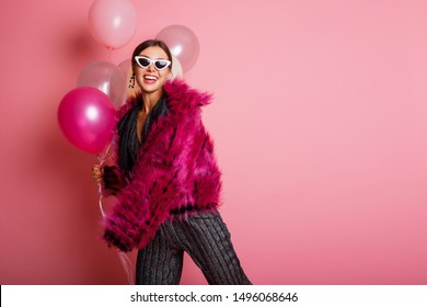 Fashionable  Happy Model  In   Winter Fur Coat  Posing On Pink Background. Dressed In  Playsuit With Sequins. White  Glasses And Earrings.  Party  Mood.  