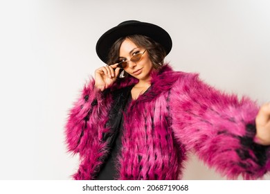 Fashionable happy model in winter pink  fur coat posing on white background.  New year party mood. Black hat. 