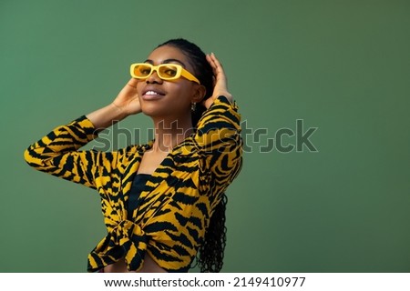 Fashionable happy smiling Black woman wearing trendy yellow rectangle sunglasses, animal, tiger print blouse, posing on green background. Copy, empty space for text