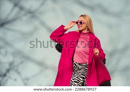 Fashionable happy smiling blonde woman wearing trendy pink sunglasses, fuchsia color coat, turtleneck, zebra print trousers, holding faux leather tote, shopper bag. Copy, empty space for text 