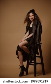 Fashionable Happy Smiling Woman Wearing Total Black Outfit With Leather Beret, Jacket, Dress, Lace Up Chunky Sole Ankle Boots. Full-length Studio Portrait 