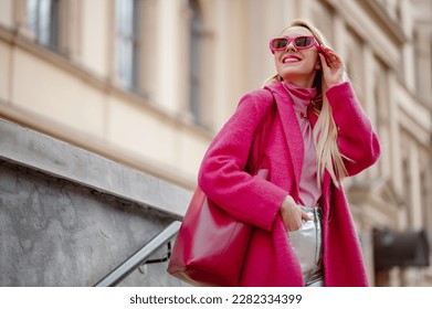 Fashionable happy smiling woman wearing fuchsia color coat, sunglasses, pink turtleneck, holding faux leather tote, shopper bag, posing in street of city. Copy, empty space for text - Powered by Shutterstock