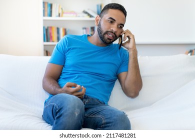 Fashionable Latin American Hipster Man With Beard Talking At Mobile Phone Indoors At Home