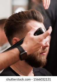 Fashionable man with a beard makes hair styling. the hairdresser sprays hairspray on the hairstyle. final touch, finishing the image.