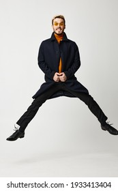 Fashionable Man In Black Coat Jumped Up With Legs Apart And Orange Sweater Copy Space. High Quality Photo