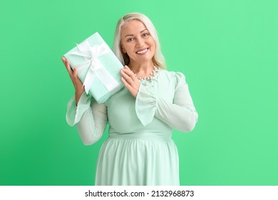 Fashionable mature woman holding gift box on green background. International Women's Day celebration