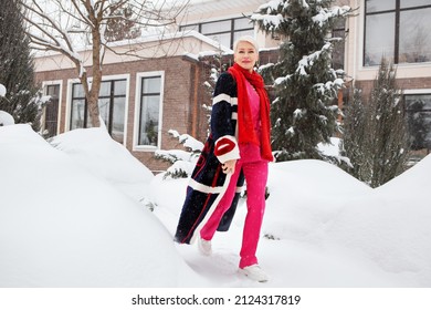 Fashionable Mature Woman Near Winter Villa House, Wealthy, Stylish And Happy Aged Female Walking At Snow Near Home. Short White Hair Model Wearing Colorful Trend Clothes