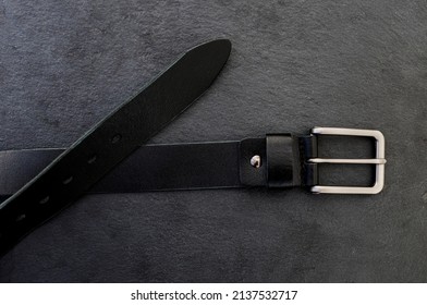 Fashionable men's black belt made of genuine leather with a light metal buckle on a dark background.