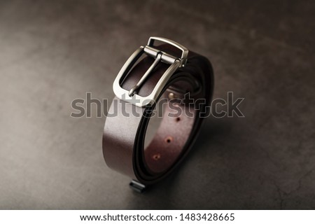 Fashionable men's brown belt made of genuine leather with a light metal buckle on a dark background. Genuine leather, handmade