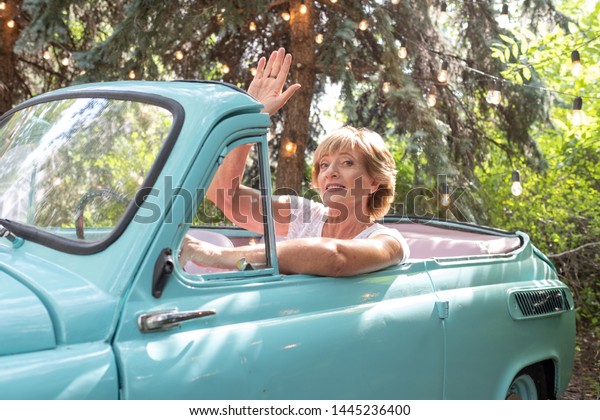 Fashionable\
modern attractive grandmother sits behind the wheel retro car.\
Summer vacation and travel of older\
people