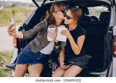 Fashionable Mother With Daughter. Family Is Sitting In The Trunk. Girl In A Black T-shirt. Ladies Eating A Donuts