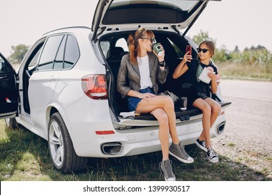 Fashionable Mother With Daughter. Family Is Sitting In The Trunk. Girl In A Black T-shirt. Ladies Eating A Donuts