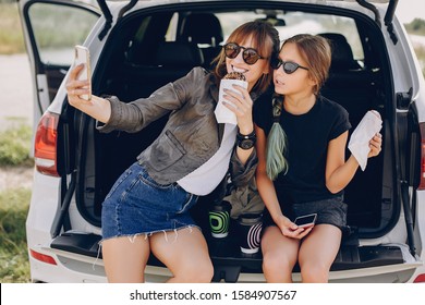 Fashionable Mother With Daughter. Family Is Sitting In The Trunk. Girl In A Black T-shirt. Ladies Eating A Donuts