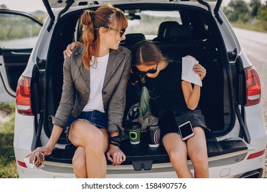 Fashionable Mother With Daughter. Family Is Sitting In The Trunk. Girl In A Black T-shirt. Ladies Eating A Donuts