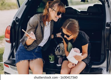 Fashionable Mother With Daughter. Family Is Sitting In The Trunk. Girl In A Black T-shirt. Ladies Eating A Donuts