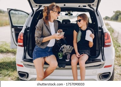 Fashionable Mother With Daughter. Family Is Sitting In The Trunk. Girl In A Black T-shirt. Ladies Eating A Donuts