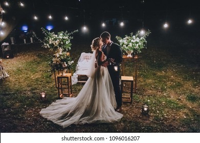 Fashionable newlyweds stand at night against the backdrop of chic decorations and flowers,electric bulbs and garlands,in the backlight. Night shooting of bride and groom.Floristics. Grain,film effect  - Powered by Shutterstock