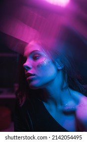 Fashionable photo of a woman with bright makeup in neon light with purple and blue in a dark room, looking away. vertical - Shutterstock ID 2142054495