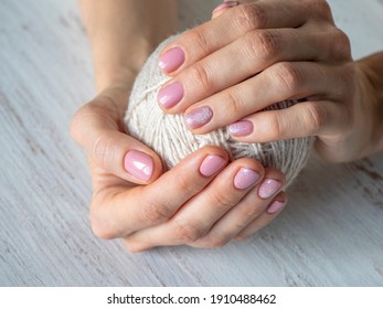 Fashionable pink manicure design in the hand. Hands are wrapped around a ball of wool.