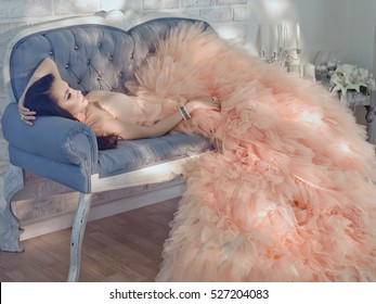 Fashionable Portrait Of Beautiful Lady In Gorgeous Couture Dress On Sofa.
Couture Elegant, Evening Dress Fashion Model Posing. Princess In Luxury Gown. Holiday Look. Morning Of Bride In Sun Room
