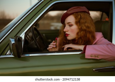 Fashionable redhead woman doing lips makeup, using marsala, dark red color lipstick, posing in the green vintage car. Copy, empty space for text
 - Powered by Shutterstock