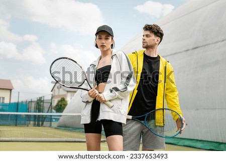 fashionable sportswear, man and woman holding tennis rackets on court,  sport and style