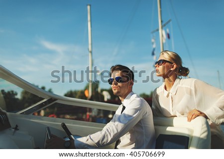 Fashionable stylish couple driving luxury yacht and posing in sunglasses with blue sky background