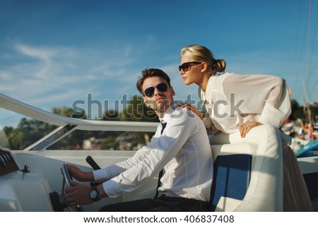 Fashionable stylish couple driving luxury motorboat yacht and posing in sunglasses with blue sky with clouds background