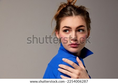 Fashionable stylish emotional woman wearing blue shirt posing over gray background. Model with vivid facial expression. Concept of fashion, style, youth, beauty. Closeup