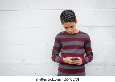 Fashionable teenage Asian boy standing alone against a white background using his smartphone.  Teen social concepts:  power of social media, addiction to social media, online social network
