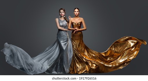 Fashionable Two Woman In Golden Evening Dress And Silver Gown. Glamour Beauty Model Fashion Prom Clothes With Train. Studio