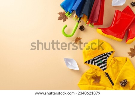 Fashionable waterproof ensemble for kids. Photograph top-down view of vibrant scene featuring colorful gum boots, a raincoat and an umbrella on a beige backdrop, leaving space for text or advertising