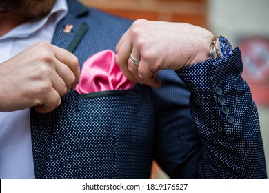 Fashionable white man wearing a watch adjusting pink handkerchief / pocket square in navy blue suit jacket