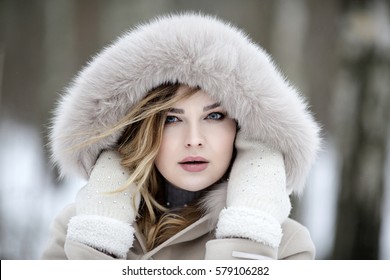 Fashionable winter portrait of lady in hat and mittens in city. Image of blonde model on bright background. Young beautiful human in colorful coat in the park with snow. Adult female person outdoors