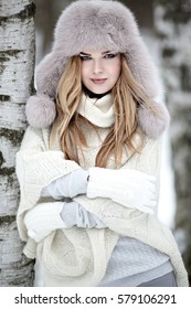 Fashionable winter portrait of lady in hat and mittens in city. Image of blonde model on bright background. Young beautiful human in colorful coat in the park with snow. Adult female person outdoors