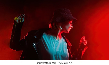 Fashionable woman dancing in red neon light, smoke background. Z generation enigmatic beautiful lady in leather jacket, panama hat, eyewear. High quality photo - Powered by Shutterstock