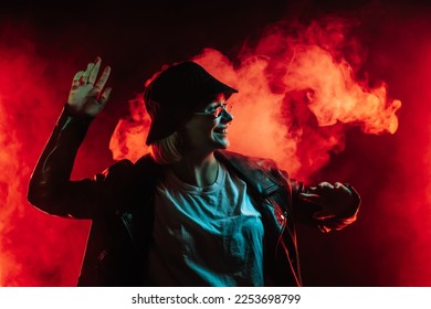 Fashionable woman dancing in red neon light, smoke background. Z generation enigmatic beautiful lady in leather jacket, bucket hat, eyewear. High quality photo - Powered by Shutterstock